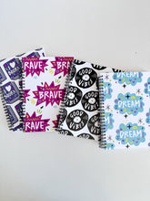 Load image into Gallery viewer, A set of four spiral bound notebooks. The notebooks feature a pattern design  with the words brave, dream, good vibes and I love books. 