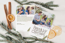 Load image into Gallery viewer, A photo of a double-sided Christmas card showing the front and back of the card laying on a white surface. Around the two sides of the card are pine needles, cinnamon sticks and dried oranges. The front of the card features a photo on the top portion and the words “Peace &amp; Joy to You This Christmas” with space to put your family name below. The back side of the card features two photos with space to write a yearly update. 