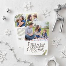 Load image into Gallery viewer, A photo of a double-sided Christmas card showing the front and back of the card laying on a white surface. Around the two sides of the card are surrounded with Christmas items. The front of the card features a photo on the top portion and the words “Peace &amp; Joy to You This Christmas” with space to put your family name below. The back side of the card features two photos with space to write a yearly update. 