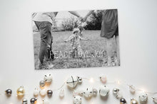 Load image into Gallery viewer, A photo of a one-sided Christmas card showing the front and back of the card laying on a white surface. To the bottom of the cards are silver and white small ornaments. The card features a photo with the words “Peace Love Joy” over the photo and a space to put your family name below. There are illustrated modern trees on the bottom. 