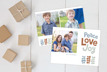 Load image into Gallery viewer, A photo of a Christmas card showing the front and back of the card laying on a white surface. Brown wrapped small gifts are to the left of the cards. The front of the card features a photo on the left side with the words “Peace Love Joy” with modern illustrated leaves below. The back of the card features two photos with the modern illustrated leaves. 