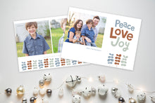 Load image into Gallery viewer, A photo of a Christmas card showing the front and back of the card laying on a white surface. To the bottom of the cards are silver and white small ornaments. The front of the card features a photo on the left side with the words “Peace Love Joy” with modern illustrated leaves below. The back of the card features two photos with the modern illustrated leaves. 
