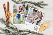 Load image into Gallery viewer, A photo of a double-sided Christmas card showing the front and back of the card laying on a white surface. Around the two sides of the card are pine needles, cinnamon sticks and dried oranges. The front of the card features a photo with the words “Peace Love joy” to the bottom right and space to the bottom left to put your family names. The words feature some modern illustrated flowers around it. The back of the card features three photos with modern illustrated flowers.