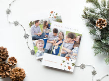 Load image into Gallery viewer, A photo of a double-sided Christmas card showing the front and back of the card laying on a white surface. Around the two sides of the card are pine cones, pine needles and a string of silver snowflake garland. The front of the card features two photos with the words “Peace. Love. Joy.” above the photos. Below the photos are colored stars and a place where you can put your family name. The back of the card features three photos and colored stars. 