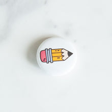 Load image into Gallery viewer, A button pin on a white tabletop. The button features an illustration of a pencil. 