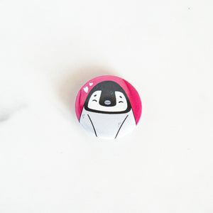 A button pin on a white tabletop. The button design features an illustrated penguin. 