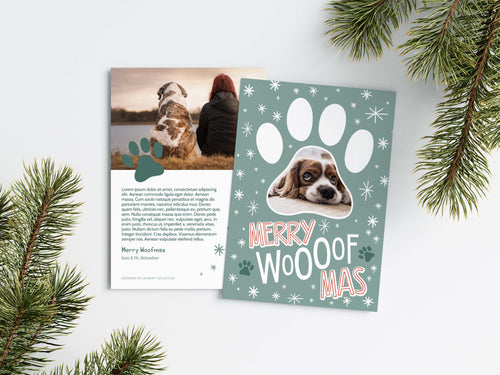 A photo of a Christmas card showing the front and back of the card laying on a white surface. Around the two sides of the card are pine needles. The front of the card features a photo inside a paw shaped frame. Around the photo are white stars and below are the words “Merry Woofmas.” The back of the card features one photo with a dog paw illustration and space to add an update. 