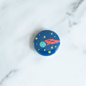 A button on a white tabletop. The button features space-themed illustration of planet. 