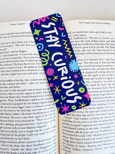 A bookmark placed inside a book. The bookmark has the words "stay curious" with fun, sketchy illustrations. 