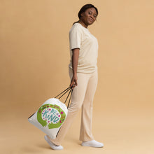 Load image into Gallery viewer, A woman walking while holding a white drawstring bag. The drawstring bag has the words &quot;Be Kind&quot; with green illustrated hands hugging the design with sketchy illustrations. 