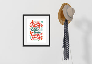 A black frame hanging on a wall with a coat rack next to it. The artwork features hand drawn lettering with the phrase "Great things never come from comfort zones."