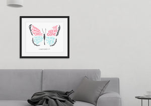 Framed artwork in a black frame on a wall above a grey sofa with a plant next to it. The hand drawn artwork features the scripture verse "Therefore, if anyone is in Christ, the new creation has come. The old has gone. The new is here." The words are featured inside a butterfly. 