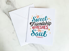 Load image into Gallery viewer, A white greeting card laying on a a marble table top with the words &quot;A Sweet Friendship Refreshes the Soul.&quot; It&#39;s shown with a white envelope. 