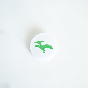 A button pin on a white tabletop. The button features an illustration of a Pterodactyl. 