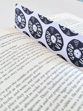 Load image into Gallery viewer, A bookmarks placed inside a book. The bookmark features the words &quot;good vibes&quot; inside an illustrated vinyl record.