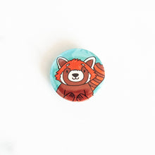 Load image into Gallery viewer, A button pin on a white tabletop. The button design features an illustrated red panda. 