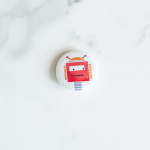 A button pin on a white tabletop. The button features an illustration of a red robot.