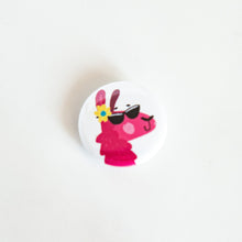 Load image into Gallery viewer, A buttons on a white tabletop. The button features a pink illustrated llama with sunglasses on a yellow flower on an ear. 