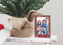 Load image into Gallery viewer, A photo of a one-sided Christmas card showing the front of the card standing up next to the bottom of a small Christmas tree with the base wrapped in burlap. The photo card features one photo with a frame of illustrated leaves in various colors. Below the photo it reads “Rejoice Greatly” and has space to put your family name. 