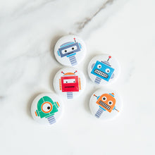 Load image into Gallery viewer, A set of five button pins on a white tabletop. The buttons feature five different illustrations of robots.