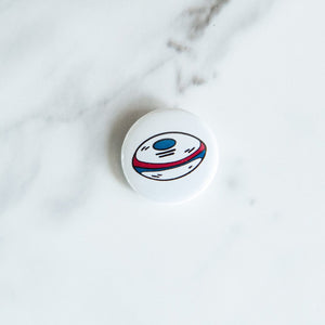 A buttons on a white tabletop. The button features an illustrations of a rugby ball. 