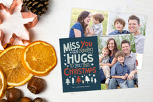 Load image into Gallery viewer, A photo of a Christmas card showing the front and back of the card laying on a white surface. Left of the card is a cookie cutter, pinecone, nuts and dried oranges. The front of the card features a photo on the right side and on the left side are the words “ Miss you and sending hugs to you this Christmas” with illustrated trees below the words. The back of the card features two photos with illustrated trees at the bottom.