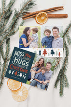 Load image into Gallery viewer, A photo of a double-sided Christmas card showing the front and back of the card laying on a white surface. Around the two sides of the card are pine needles, cinnamon sticks and dried oranges. The front of the card features a photo on the right side and on the left side are the words “ Miss you and sending hugs to you this Christmas” with illustrated trees below the words. The back of the card features two photos with illustrated trees at the bottom.
