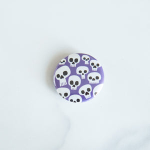 A button on a white tabletop. The button features an illustration of skeletons.