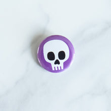 Load image into Gallery viewer, A button on a white tabletop. The button features an illustration of a skull.