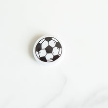 Load image into Gallery viewer, A buttons on a white tabletop. The button features an illustrations of a soccer/football. 