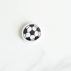 A buttons on a white tabletop. The button features an illustrations of a soccer/football. 