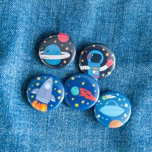 Load image into Gallery viewer, A set of five buttons on a jean jacket. The buttons feature space-themed illustrations of planets, a spaceship, a rocket and an astronaut. 