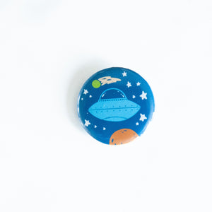 A button on a white tabletop. The button features space-themed illustration of planet. 