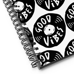 A close up of the spiral notebook binding. The pattern design features the words "good vibes" inside an illustrated vinyl record.  