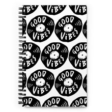 Load image into Gallery viewer, A spiral notebook is on a tabletop. The white spiral notebook has black spiral binding. The pattern design features the words &quot;good vibes&quot; inside an illustrated vinyl record.  