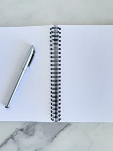 An image showing the notebook opened to show the inside pages. A pen is laying on the notebook. 