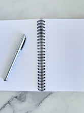 Load image into Gallery viewer, An image showing the notebook opened to show the inside pages. A pen is laying on the notebook. 