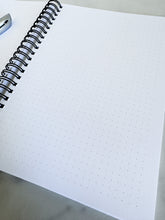 Load image into Gallery viewer, An image showing the notebook opened to show the inside pages. A pen is laying on the notebook. 