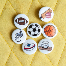 Load image into Gallery viewer, A set of buttons on a yellow background. The buttons feature illustrations of an American football, a soccer/football, a baseball with baseball bat, a rugby ball, a cricket ball and bat, a basketball and a golf club with ball. 