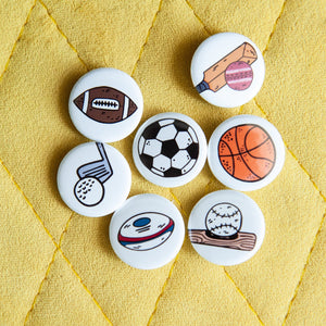 A set of buttons on a yellow background. The buttons feature illustrations of an American football, a soccer/football, a baseball with baseball bat, a rugby ball, a cricket ball and bat, a basketball and a golf club with ball. 