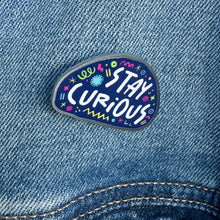 Load image into Gallery viewer, An enamel pin on a jean jacket with the words &quot;stay curious&quot; surrounded by whimsical sketches. 