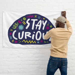 A man hanging a large white flag on a wall. The white flag features the words "stay curious" featured inside a a purple shape with sketchy illustrations around. 