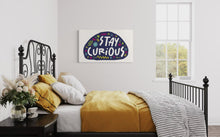 Load image into Gallery viewer, A large flag featured on the wall of a bedroom. The white flag features the words &quot;stay curious&quot; featured inside a a purple shape with sketchy illustrations around. 