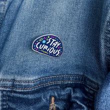 Load image into Gallery viewer, An enamel pin on a jacket with the words &quot;stay curious&quot; surrounded by whimsical sketches. 