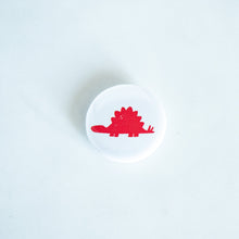 Load image into Gallery viewer, A button pin on a white tabletop. The button features an illustration of a Stegosaurus. 