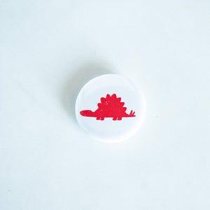 A button pin on a white tabletop. The button features an illustration of a Stegosaurus. 