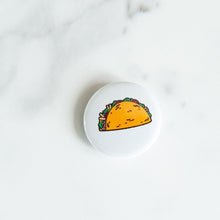 Load image into Gallery viewer, A button pin on a white tabletop. The pin features an illustration of a taco.