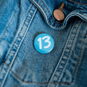 A badge on a jean jacket with a blue background and the number 13 in white. 