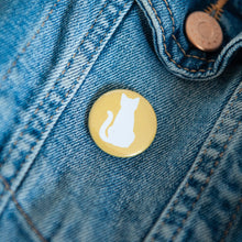 Load image into Gallery viewer, A badge on a jean jacket with a yellow background and a cat illustration in white. 