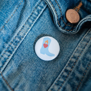 A badge on a jean jacket with a white background and a light blue cowboy boot illustration. 